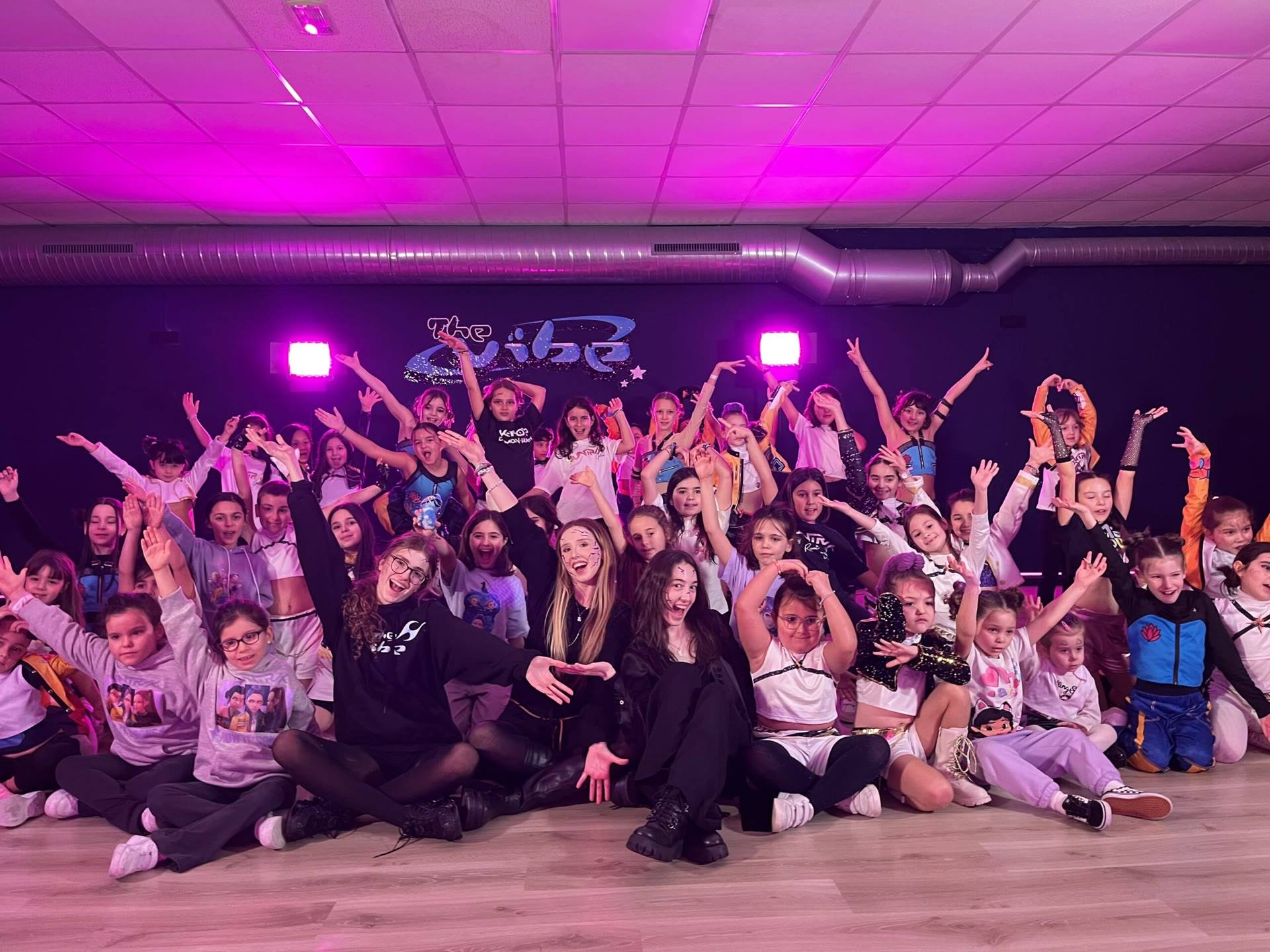 Grupo numeroso de alumnas y alumnos posando en el aula con luces rosas