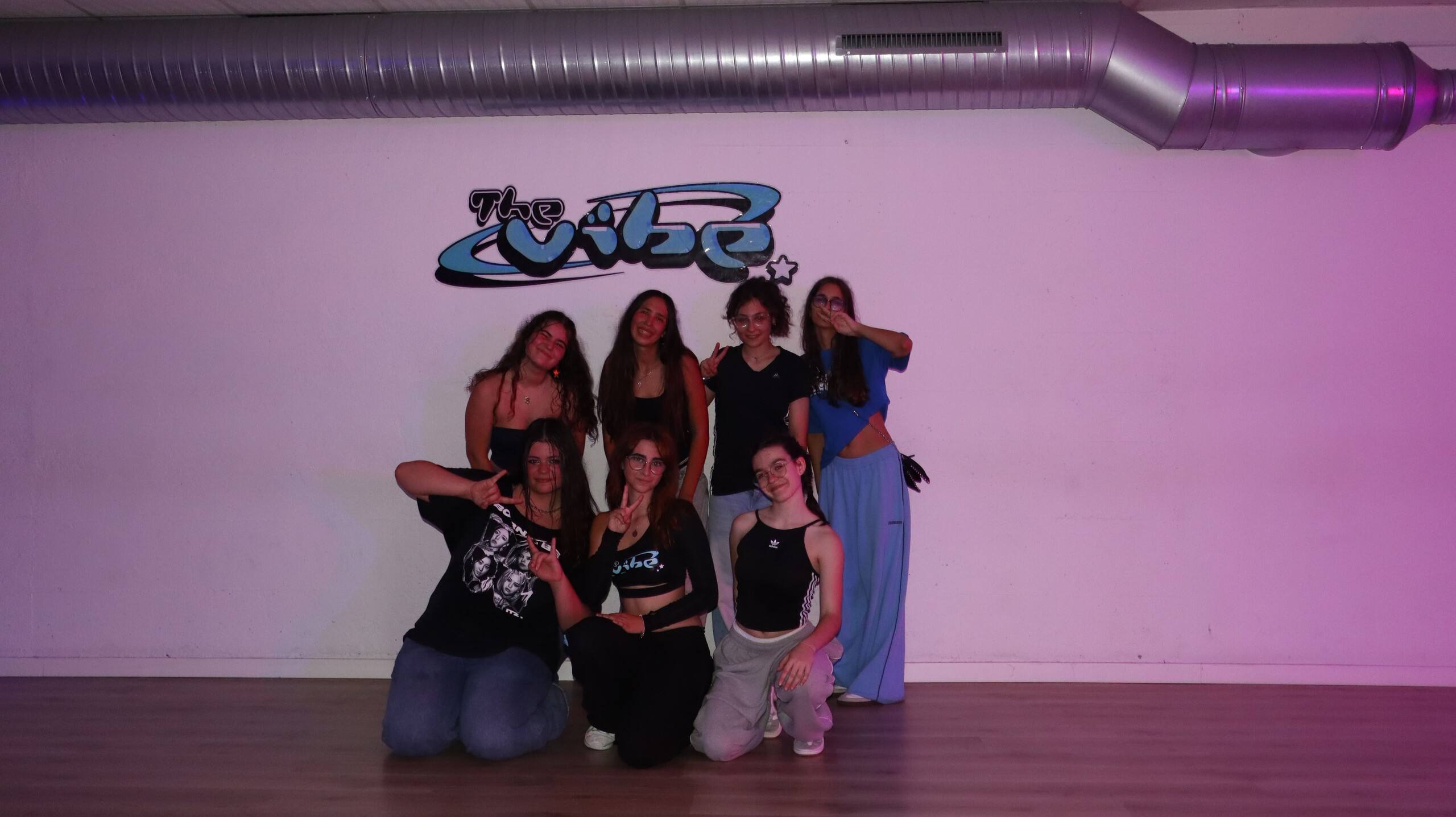 Grupo de alumnas posando bajo el logo de The Vibe en el aula